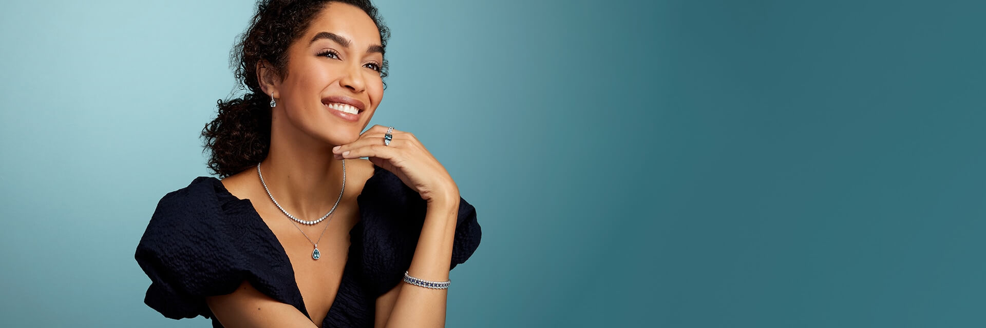 Woman smiling in gold jewelry with diamonds and blue topaz gemstones.
