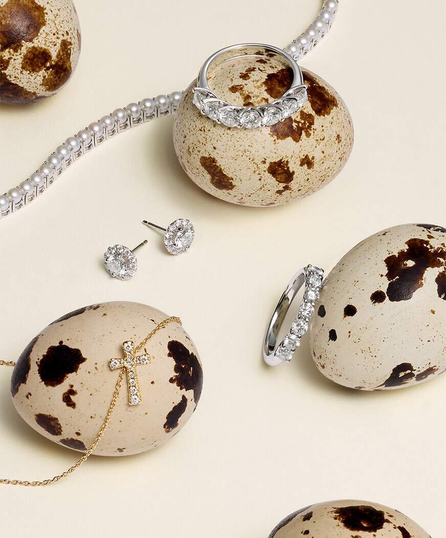 Diamond rings, earrings, and a cross necklace displayed on speckled Easter eggs.