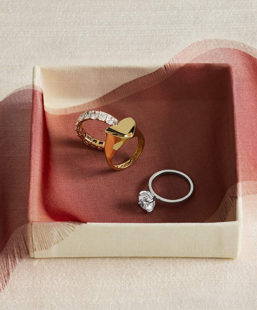 A gold heart ring and a diamond solitaire, on a fabric-lined tray.