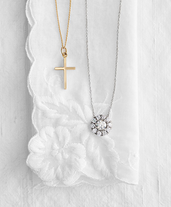 Gold cross and diamond halo pendant necklaces displayed on a white embroidered lace handkerchief
