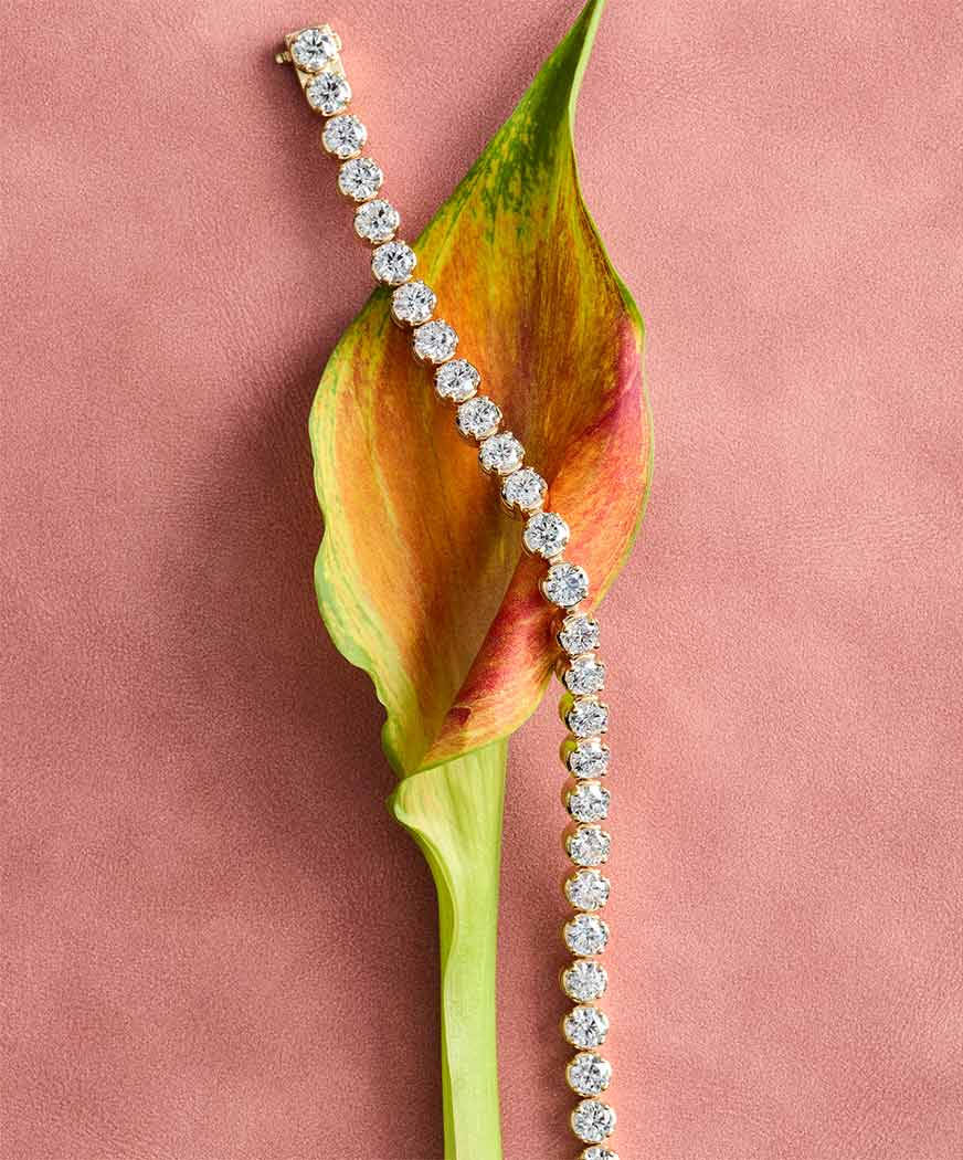Classic diamond tennis bracelet in 14k yellow gold draped over a fresh white Calla Lily flower