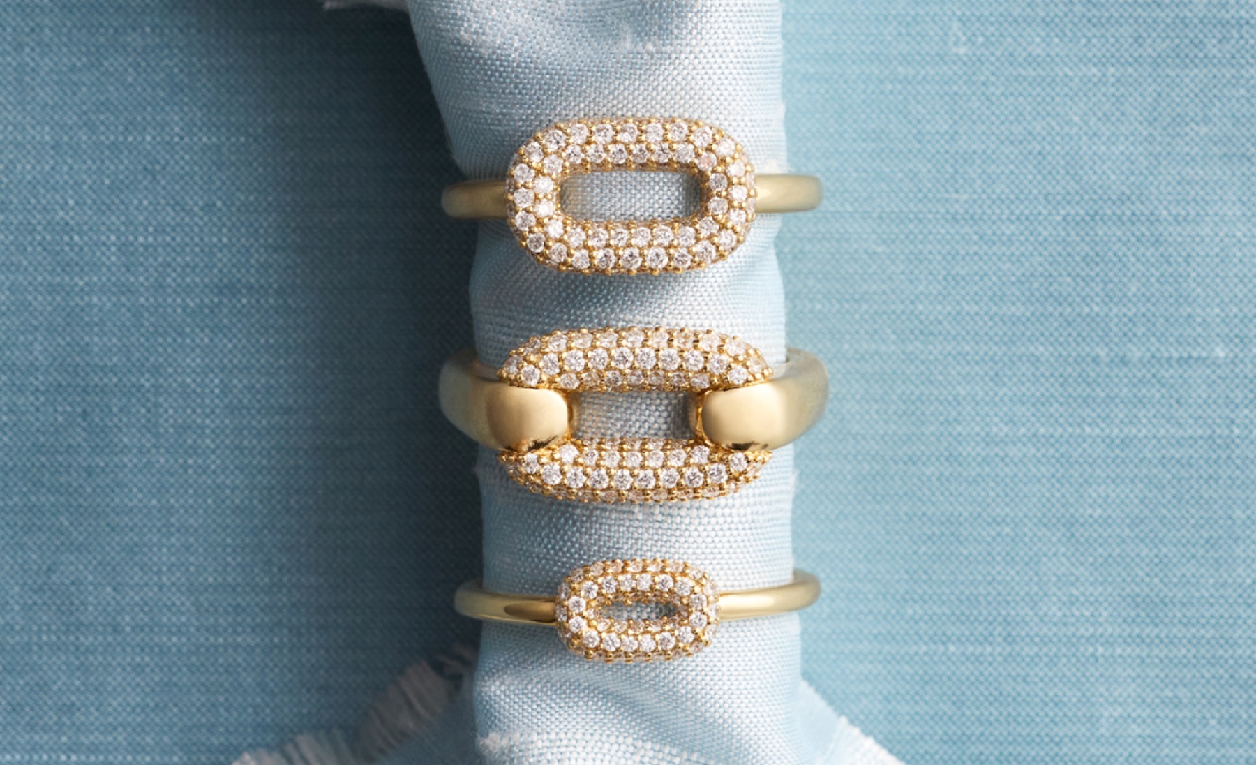 Three stacked Ellipse diamond rings in 14k gold displayed on rolled fabric with pavé oval design Blue Nile